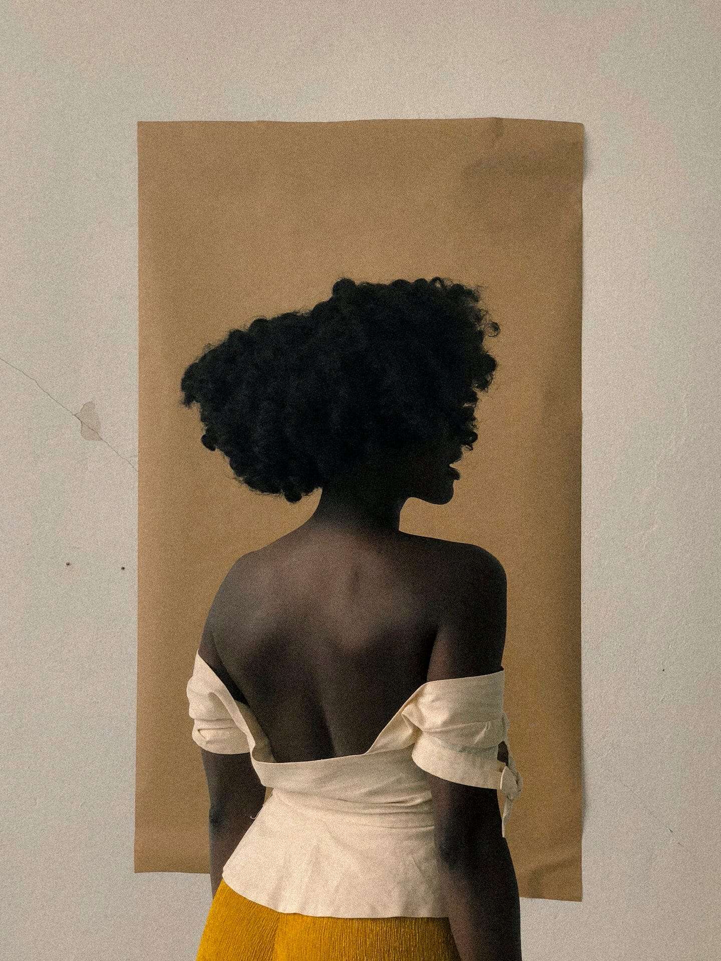 A woman seen from behind in an off-shoulder white top, before a sheet of brown paper, from Abena, photographed by Deun Ivory for Radiant Health