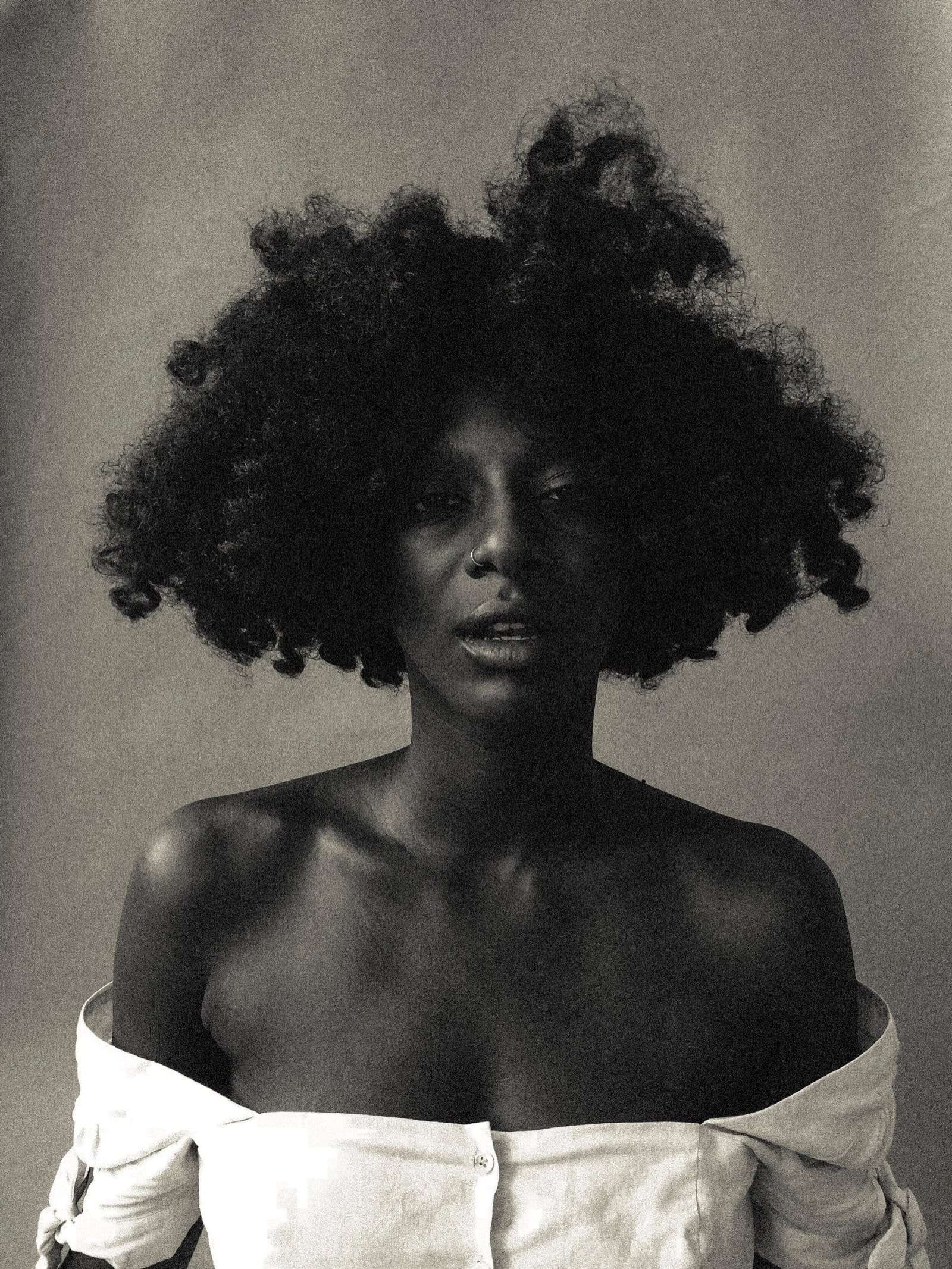 A black-and-white portrait of a woman with a full afro in an off-shoulder white top, from Abena, photographed by Deun Ivory for Radiant Health