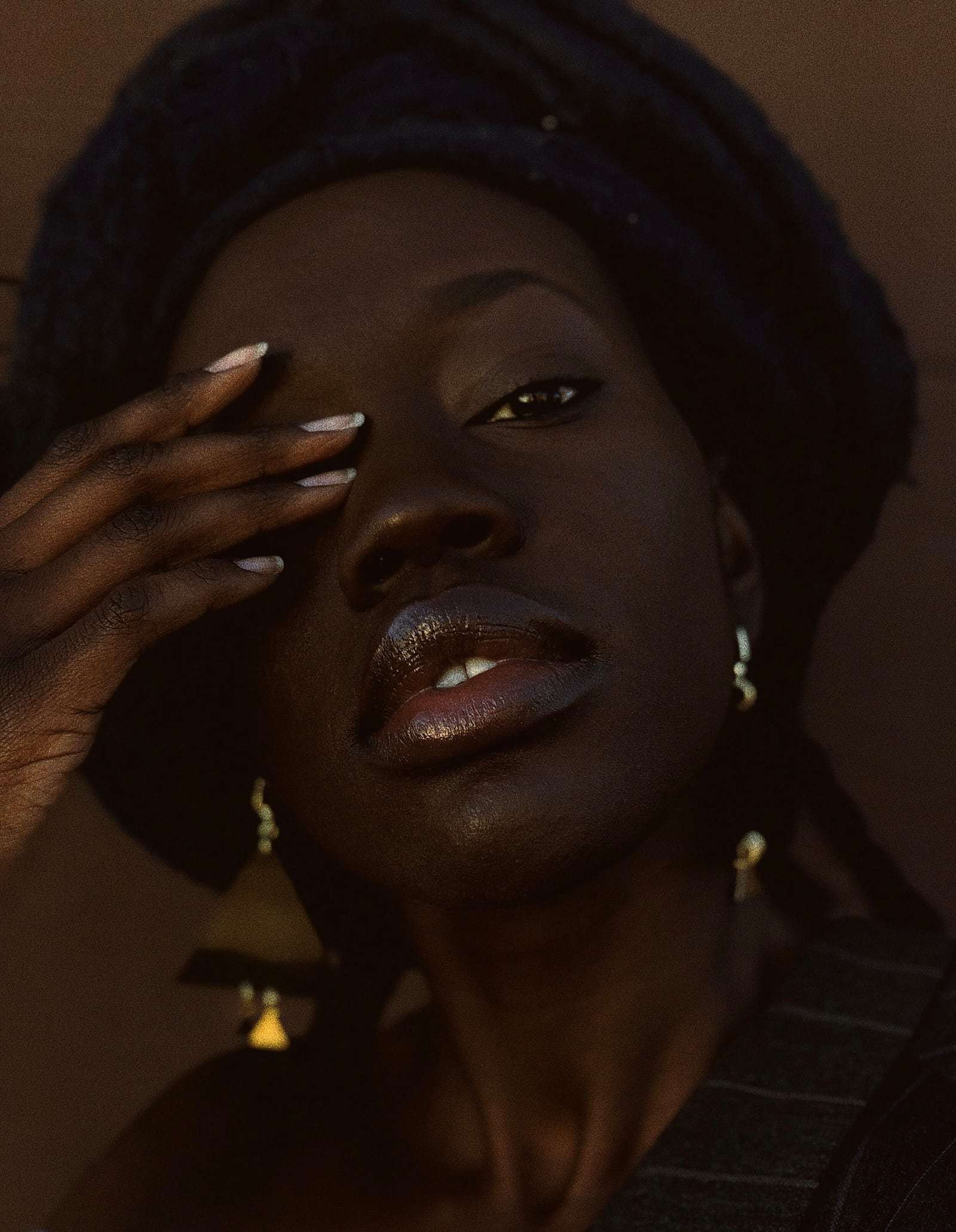 A woman in a dark head wrap touching her brow, in warm low light, from Deun Ivory’s global campaign for Apple