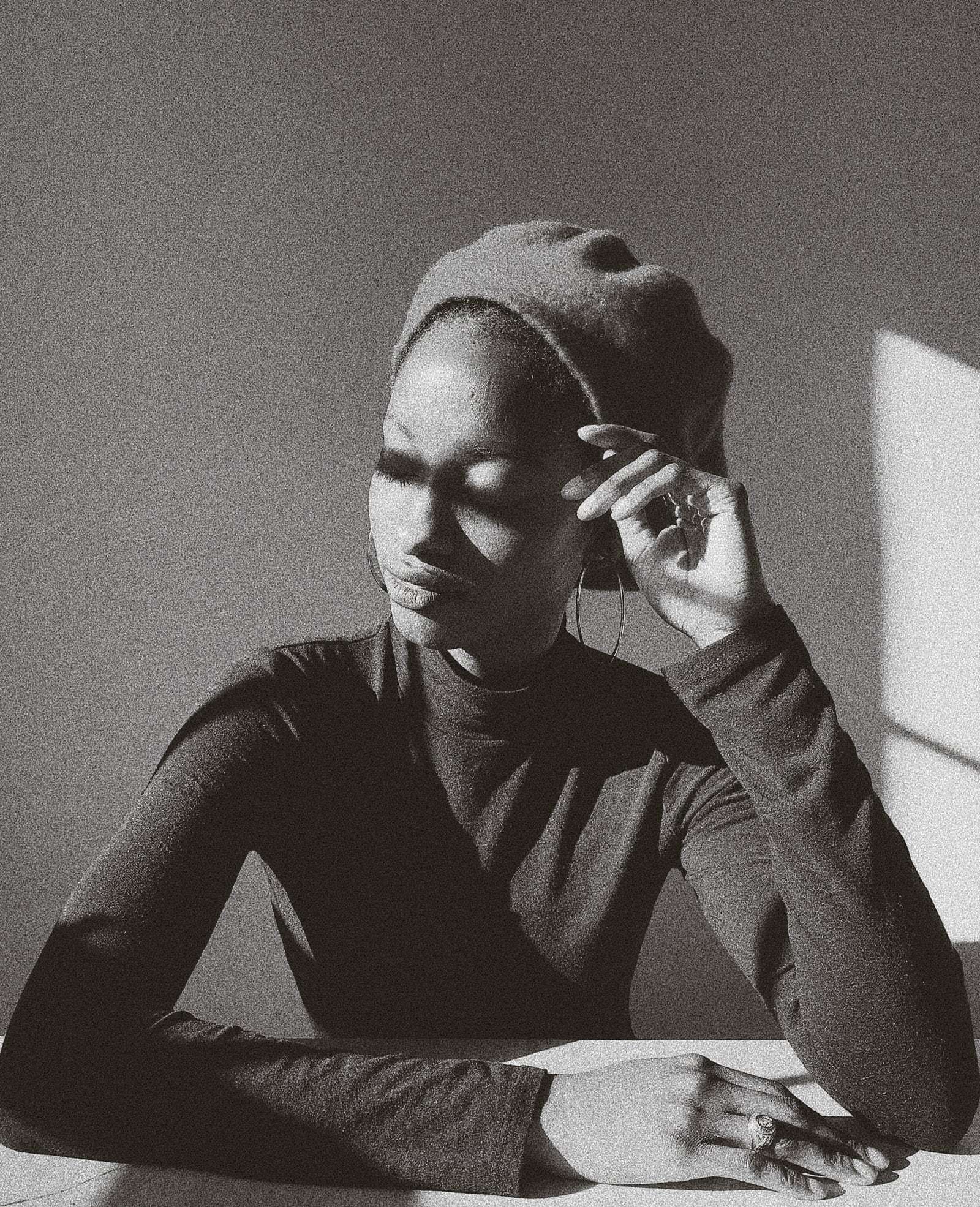 A woman in a beret resting her head on her hand by a sunlit wall, in black and white, from Deun Ivory’s global campaign for Apple