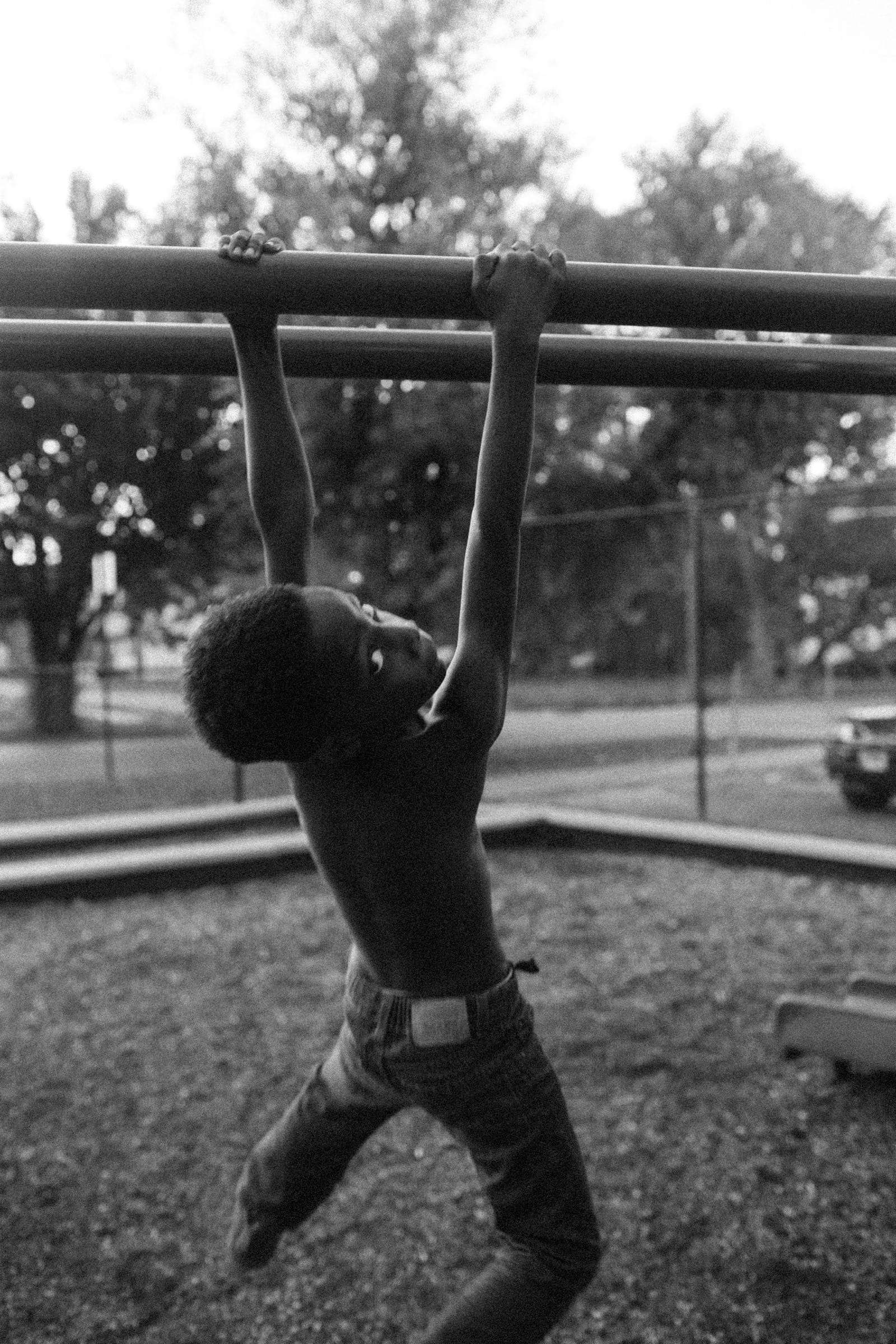 A boy hanging from playground bars, in black and white, from Black Boy Joy, a series by Deun Ivory