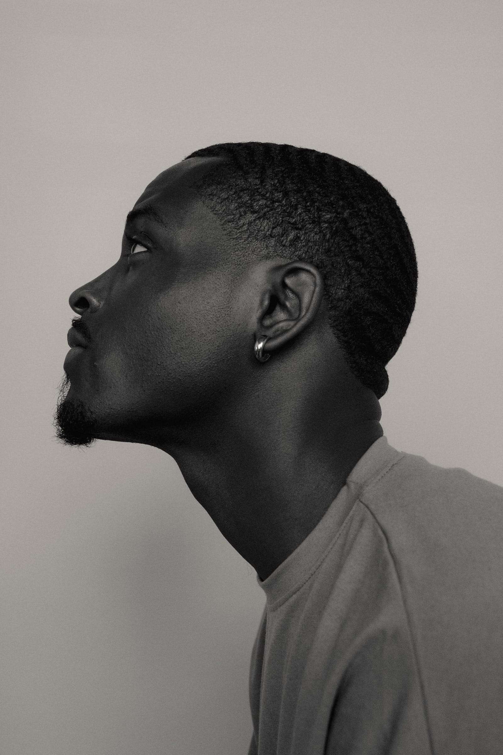 A man in profile, chin raised, against a pale grey wall, from Day Dream, a series by Deun Ivory