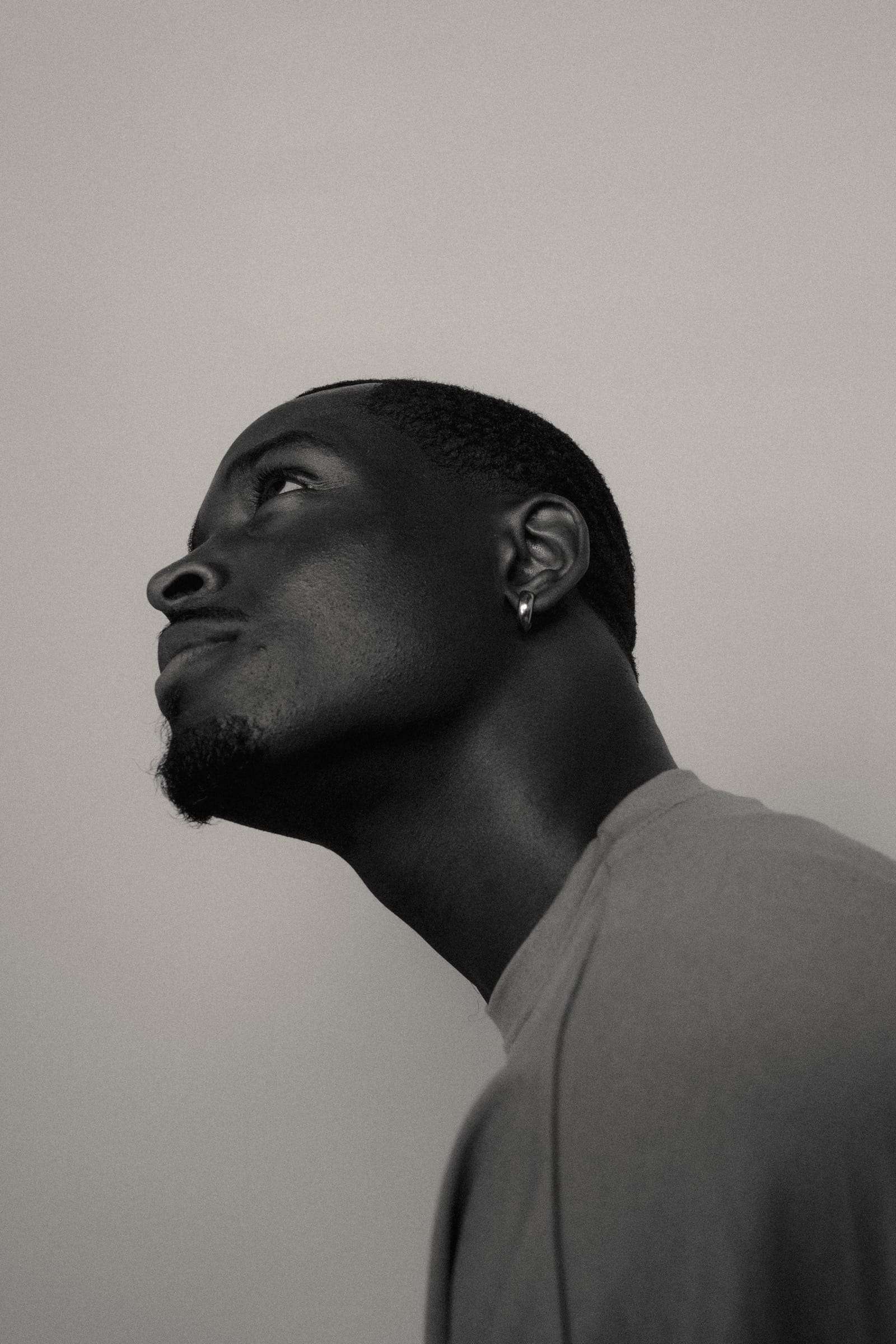 A man with his head tipped back, eyes lowered, against a pale grey wall, from Day Dream, a series by Deun Ivory