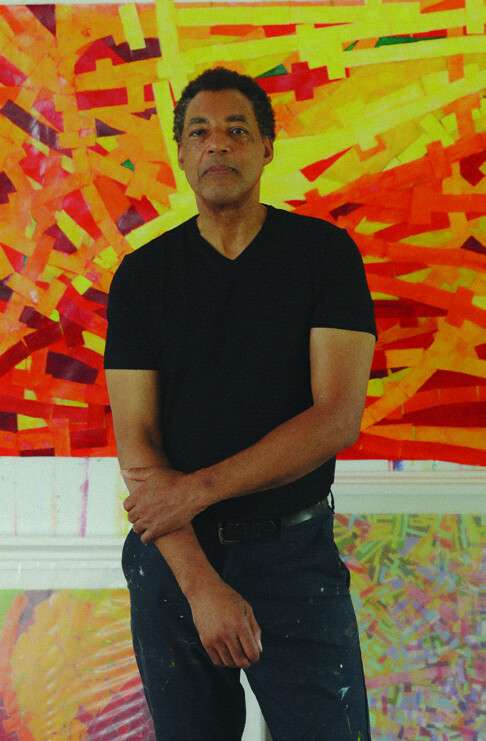 Rick Lowe standing in front of an orange painting in his studio, photographed by Deun Ivory