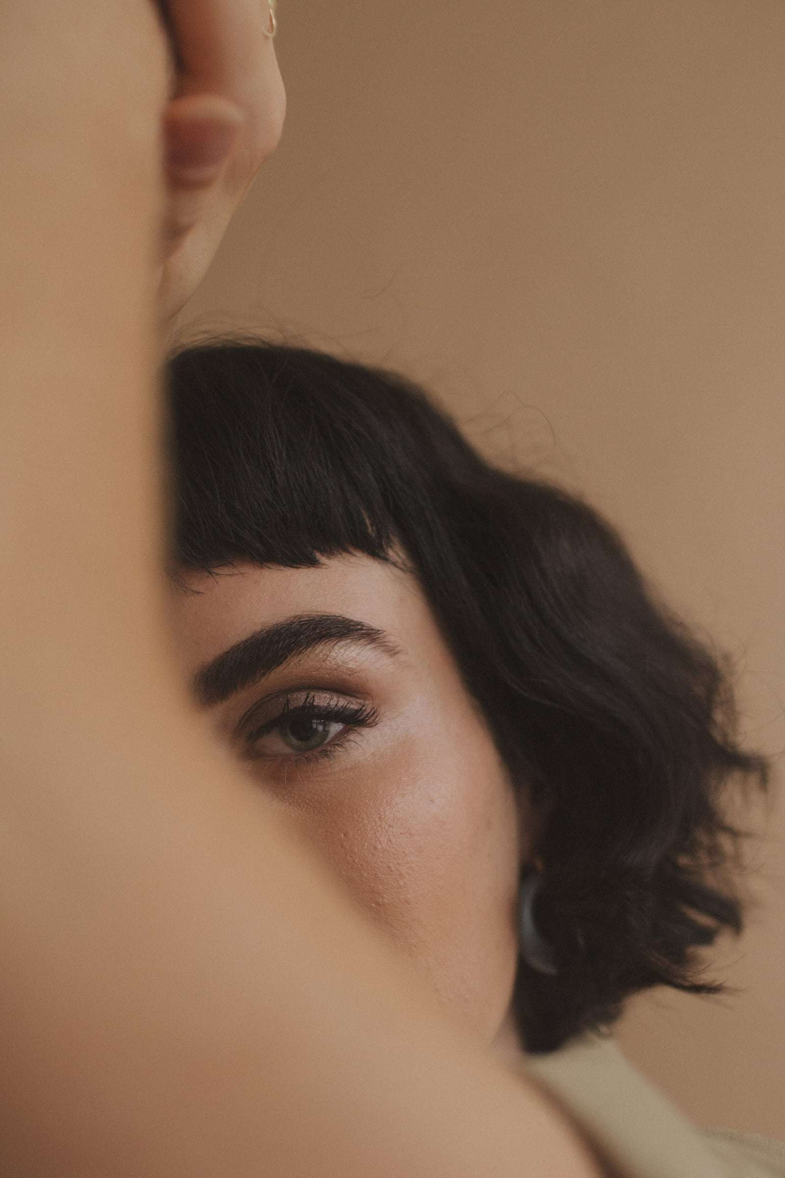 A woman with a fringe, half hidden behind a raised arm, from Deun Ivory’s campaign for Glossier