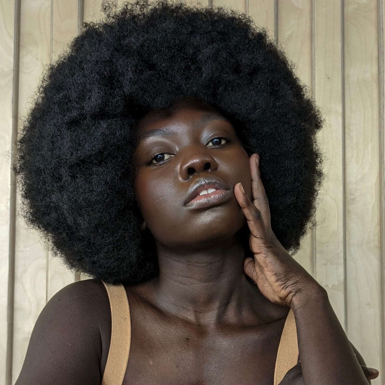 A woman with a full afro, hand to her cheek, against pale wood panels, from Deun Ivory’s campaign for Google Pixel
