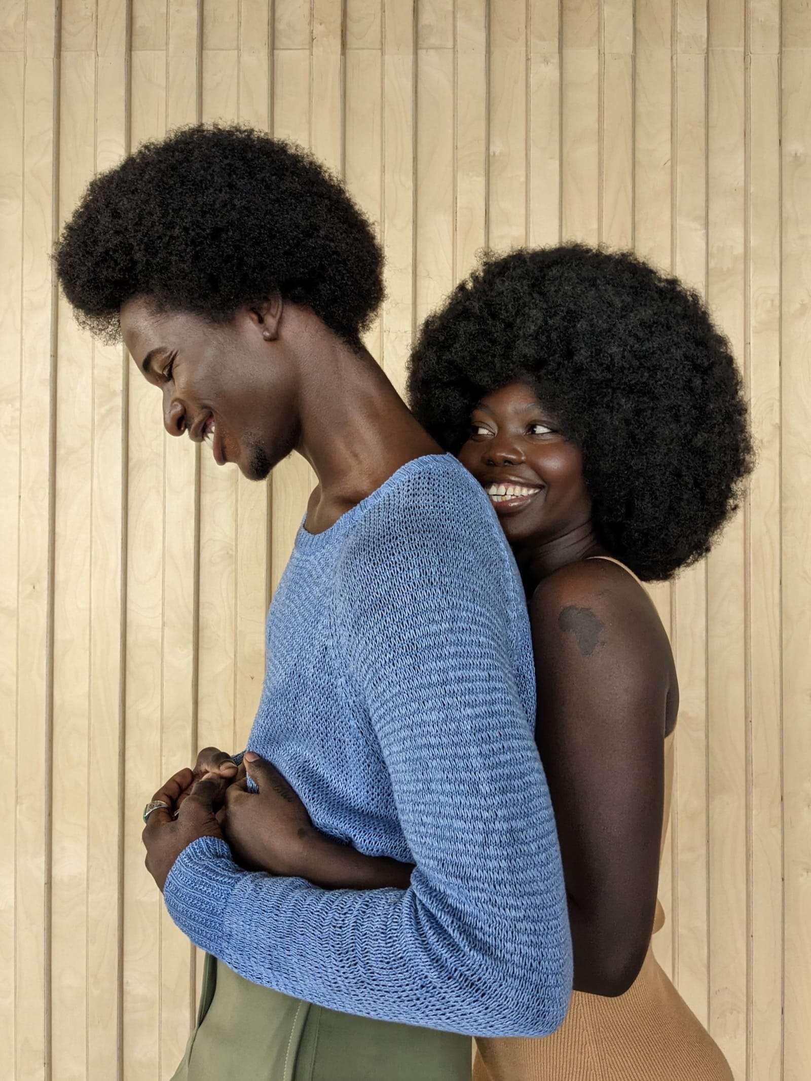 Two people embracing, one in a blue knit sweater, against pale wood panels, from Deun Ivory’s campaign for Google Pixel