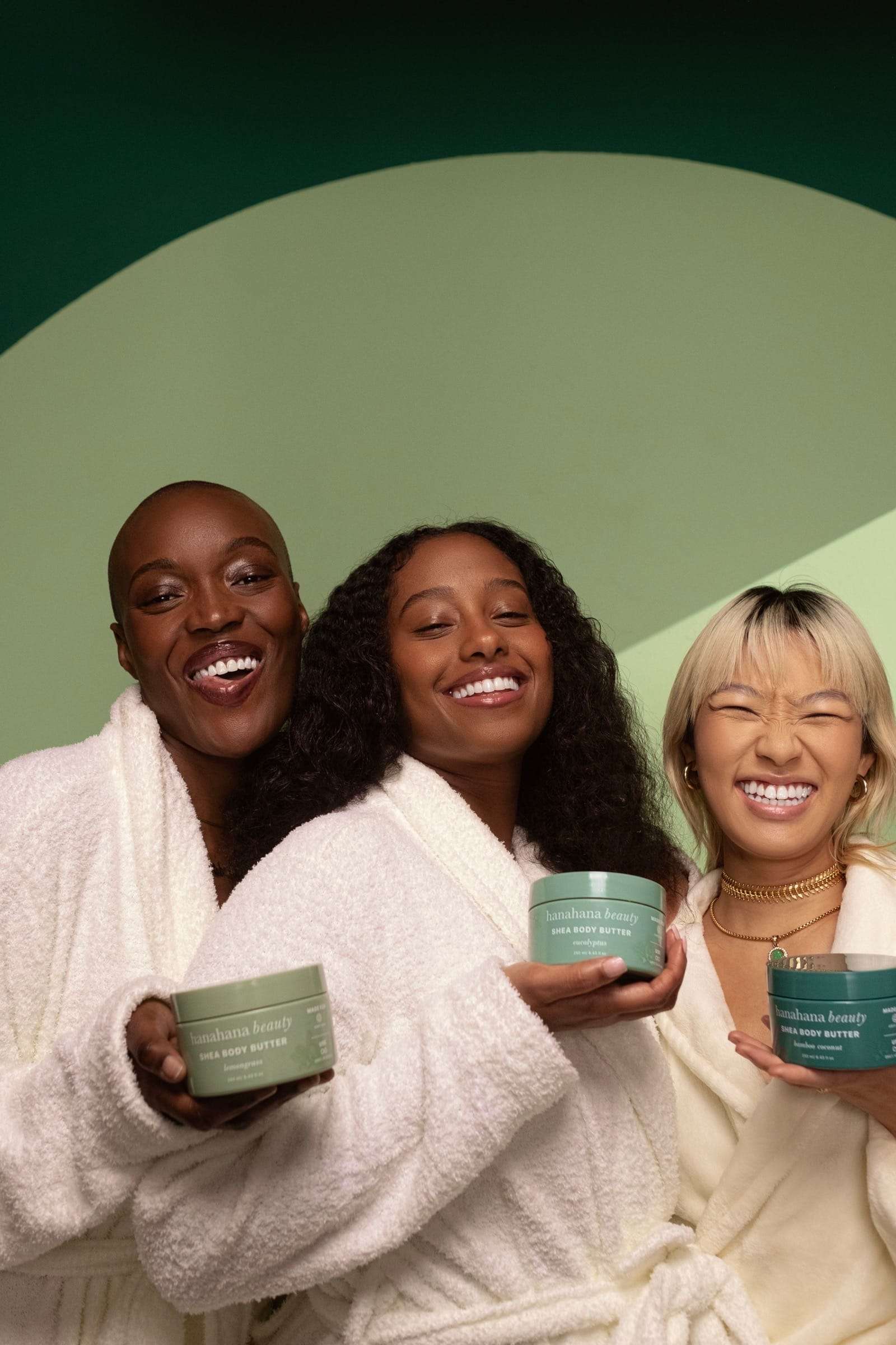 Three women in white robes holding jars of body butter before a green arch, from Deun Ivory’s campaign for Hanahana Beauty at ULTA