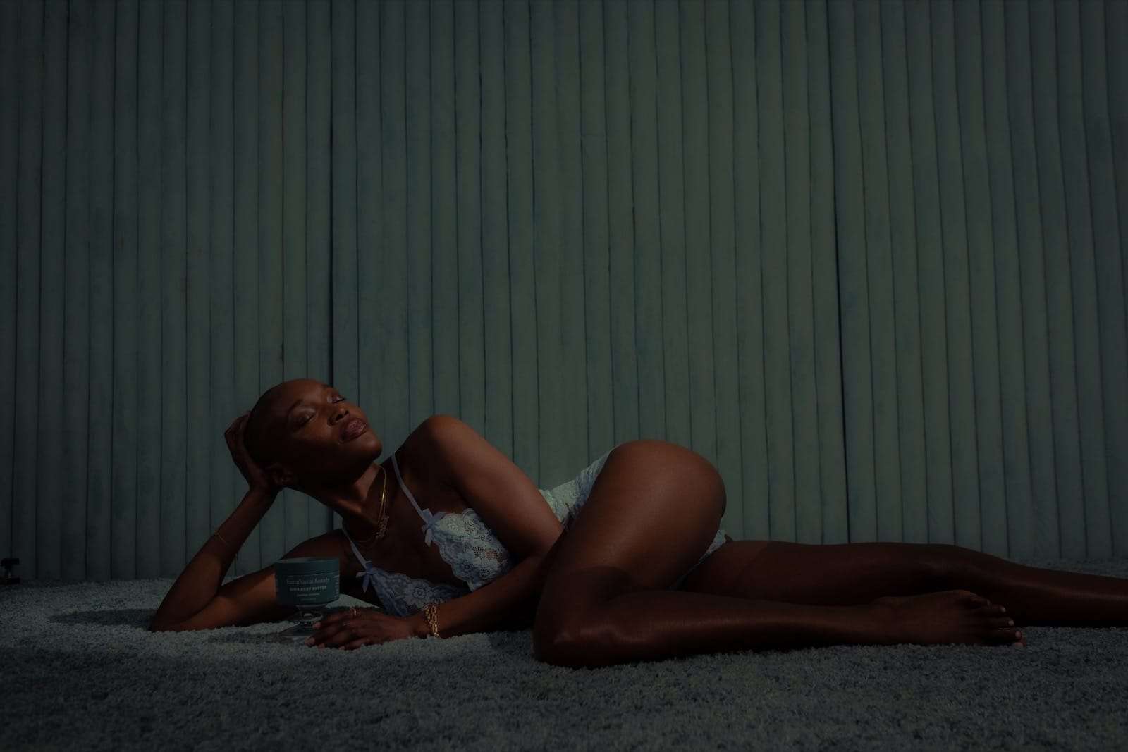A woman reclining on a dark green carpet before a green curtain, from Deun Ivory’s campaign for Hanahana Beauty at ULTA