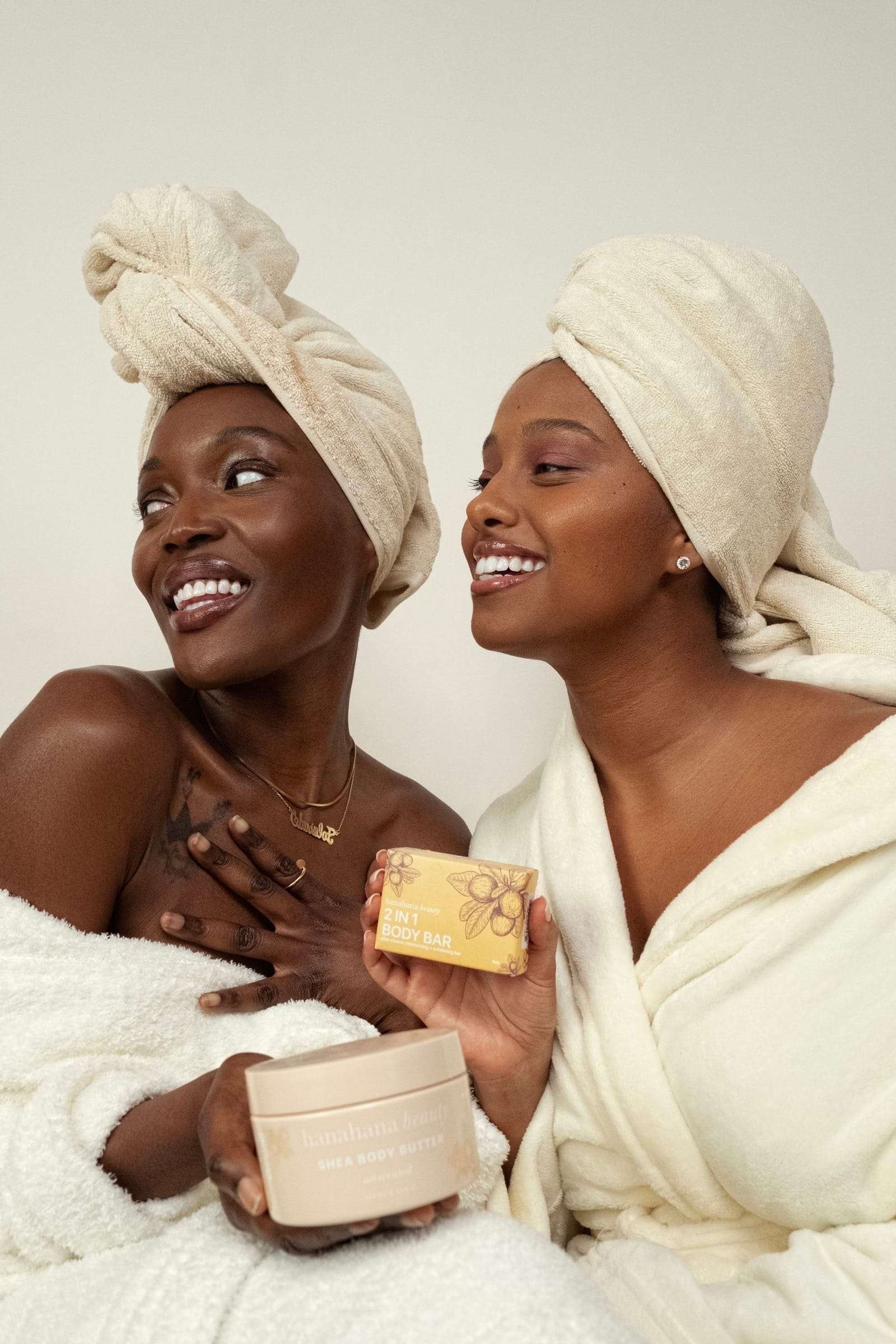 Two women in towel turbans and robes laughing, holding jars of body butter, from Deun Ivory’s campaign for Hanahana Beauty at ULTA