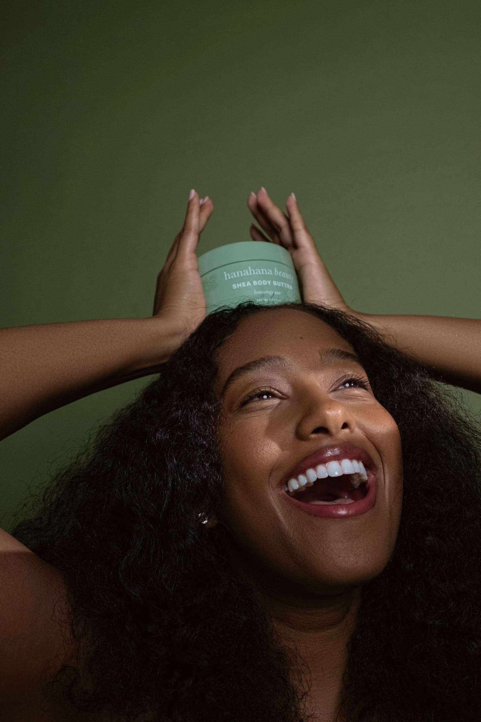 A laughing woman balancing a jar of body butter on her head, from Deun Ivory’s campaign for Hanahana Beauty at ULTA
