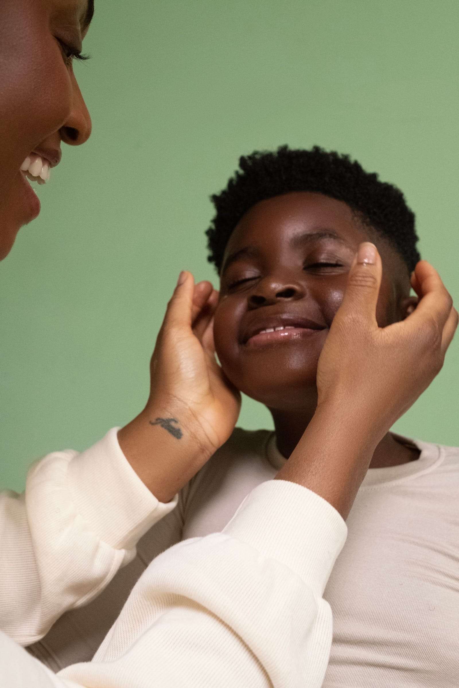 Hands cupping the face of a smiling young man, against a green wall, from Deun Ivory’s campaign for Hanahana Beauty at ULTA