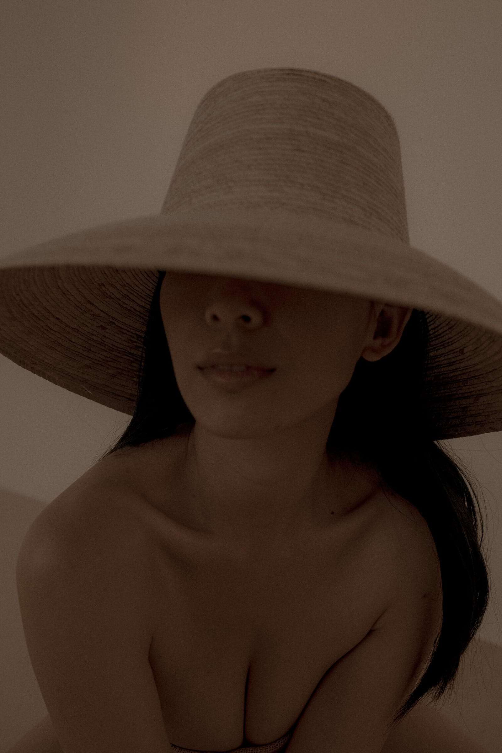 A woman in a wide straw hat, its brim hiding her eyes, in soft warm light, from Deun Ivory’s campaign for Honeynsilk