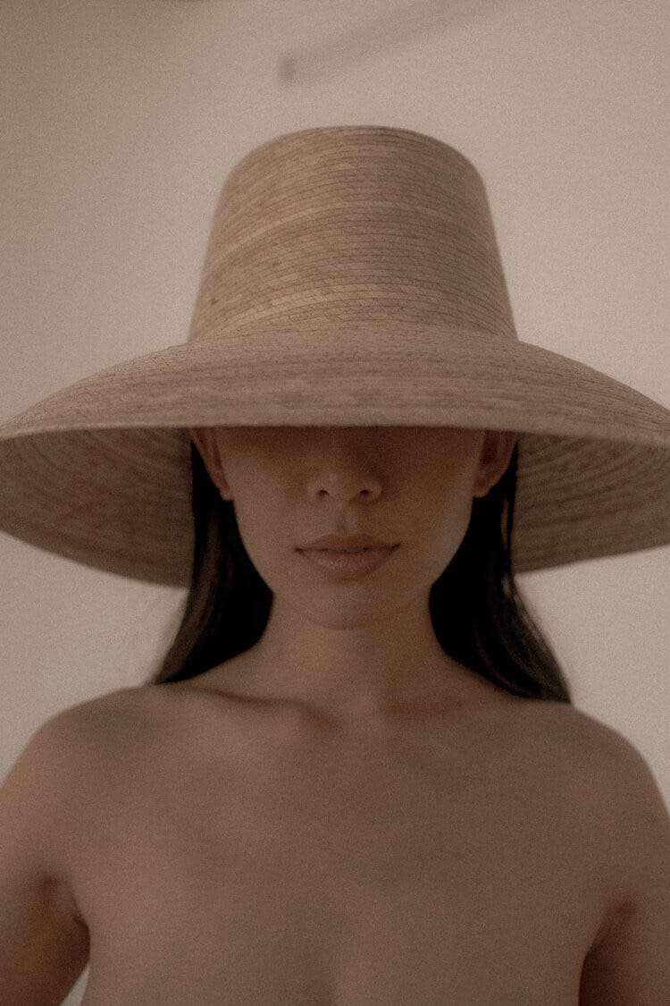 A woman facing the camera, a wide straw hat shading her eyes, from Deun Ivory’s campaign for Honeynsilk