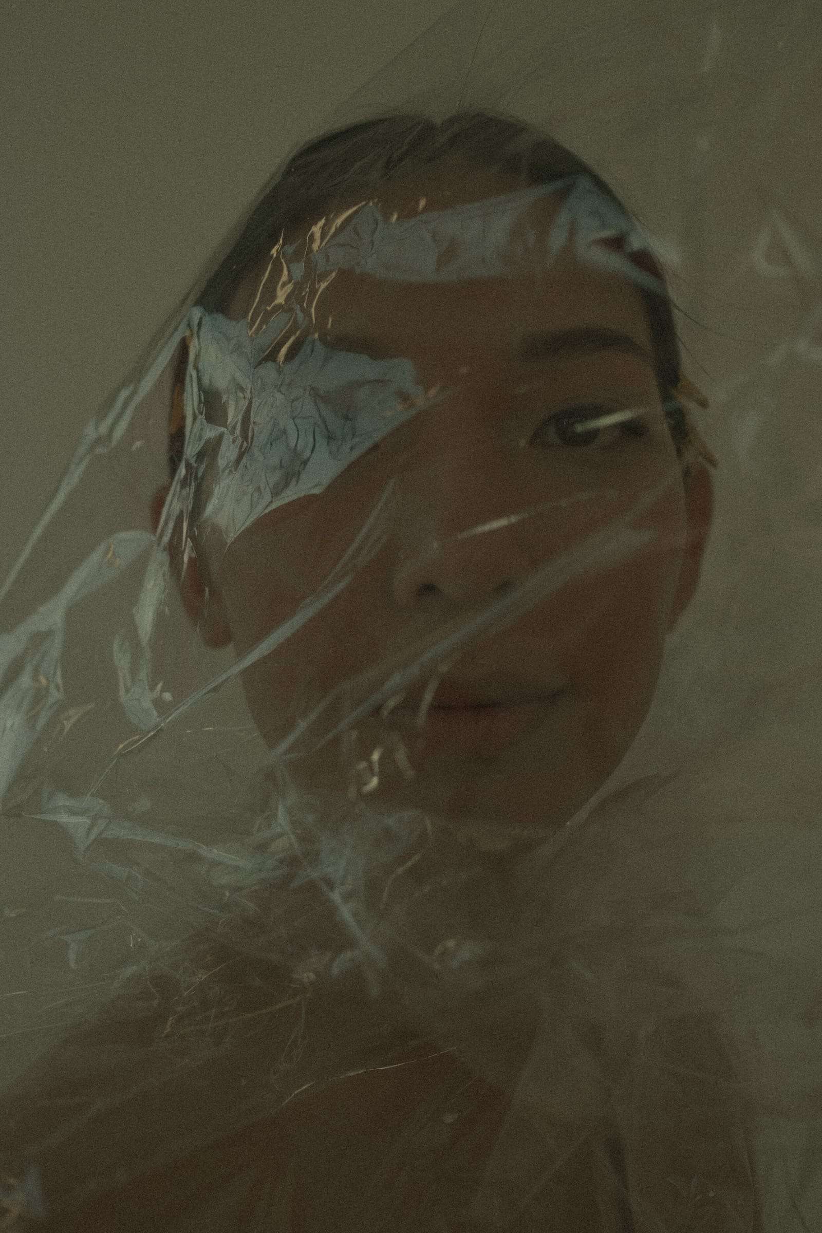 A woman’s face behind a sheet of clear plastic, in olive light, from Deun Ivory’s campaign for Honeynsilk