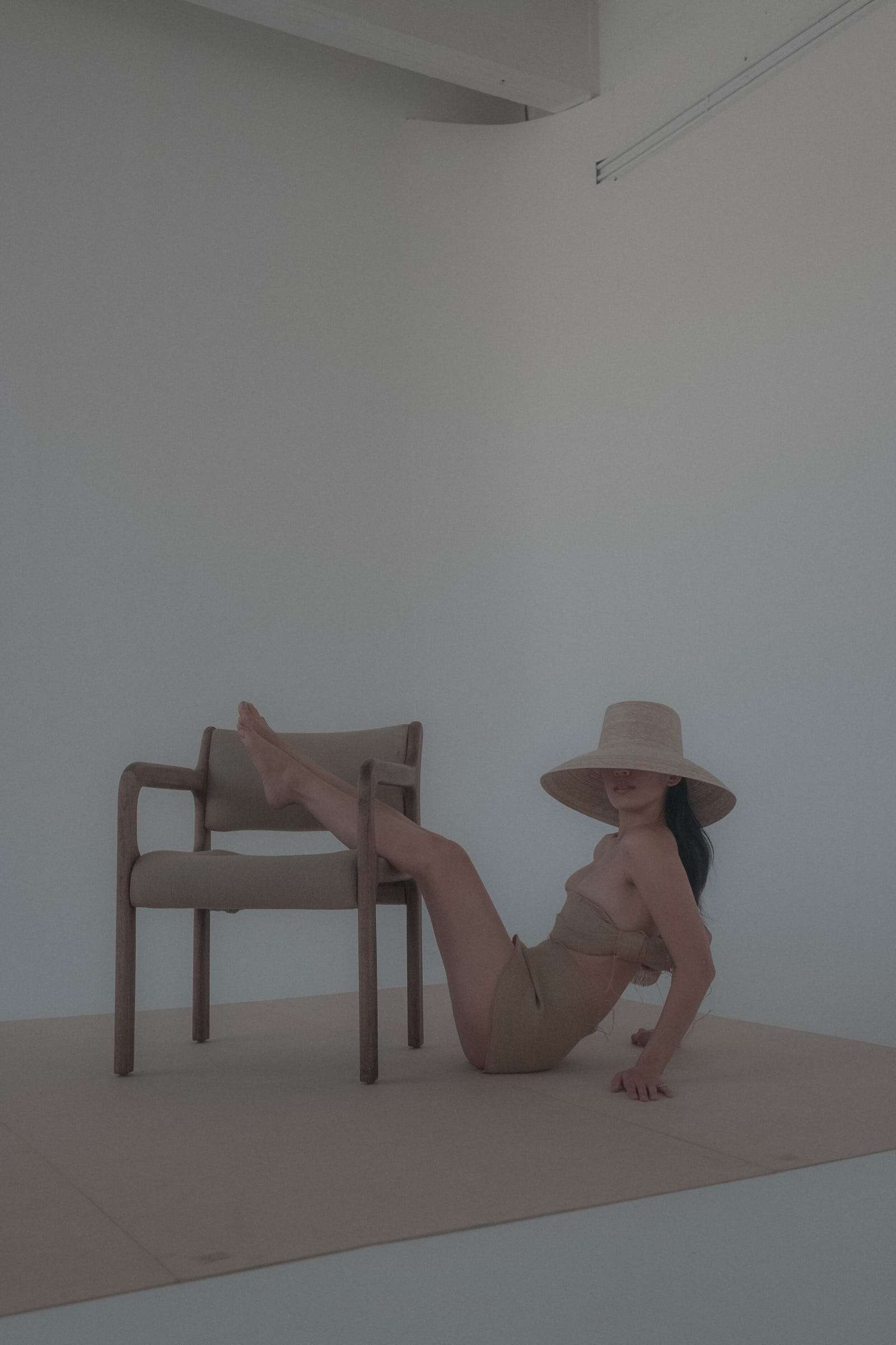 A woman in a straw hat reclining by a wooden chair, her legs on its seat, from Deun Ivory’s campaign for Honeynsilk