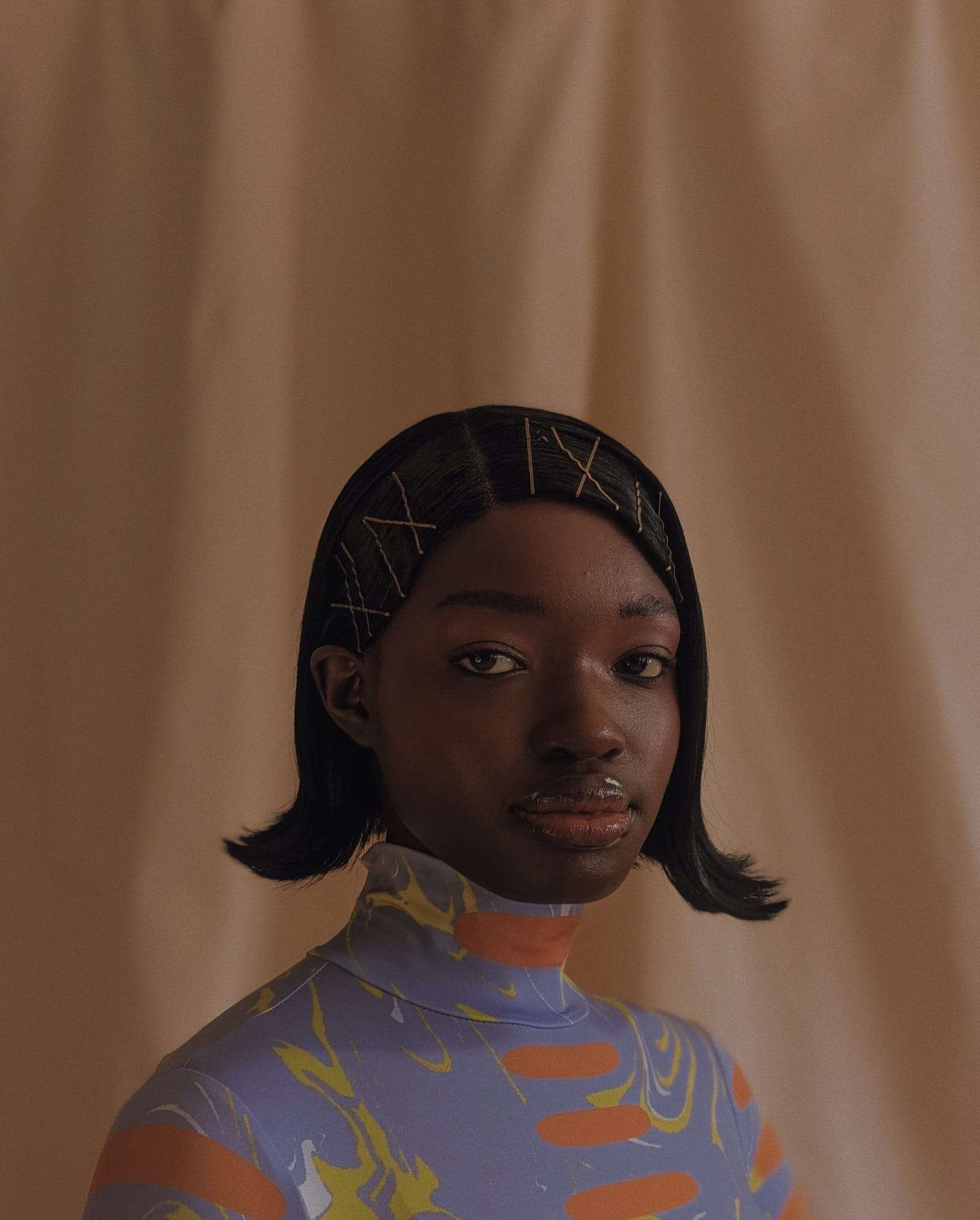 A young woman with a bob and hair clips, in a patterned top, before a peach curtain, from Project Douglas, Deun Ivory’s work with Google
