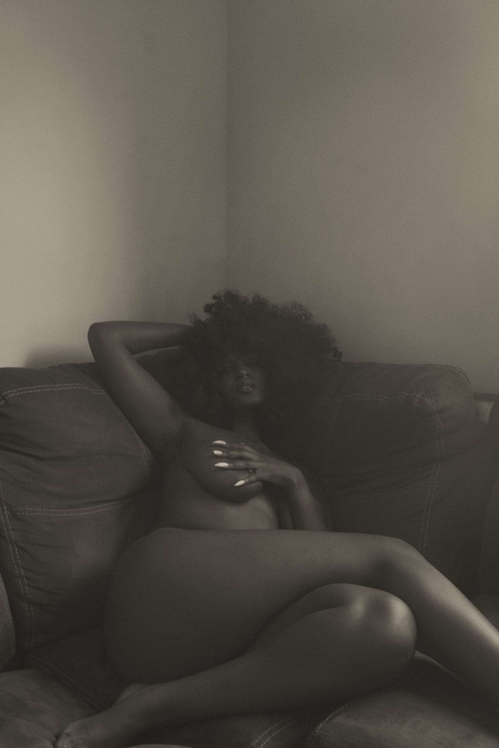 A woman reclining on a leather sofa in a dim room, from Simi, photographed by Deun Ivory for the body