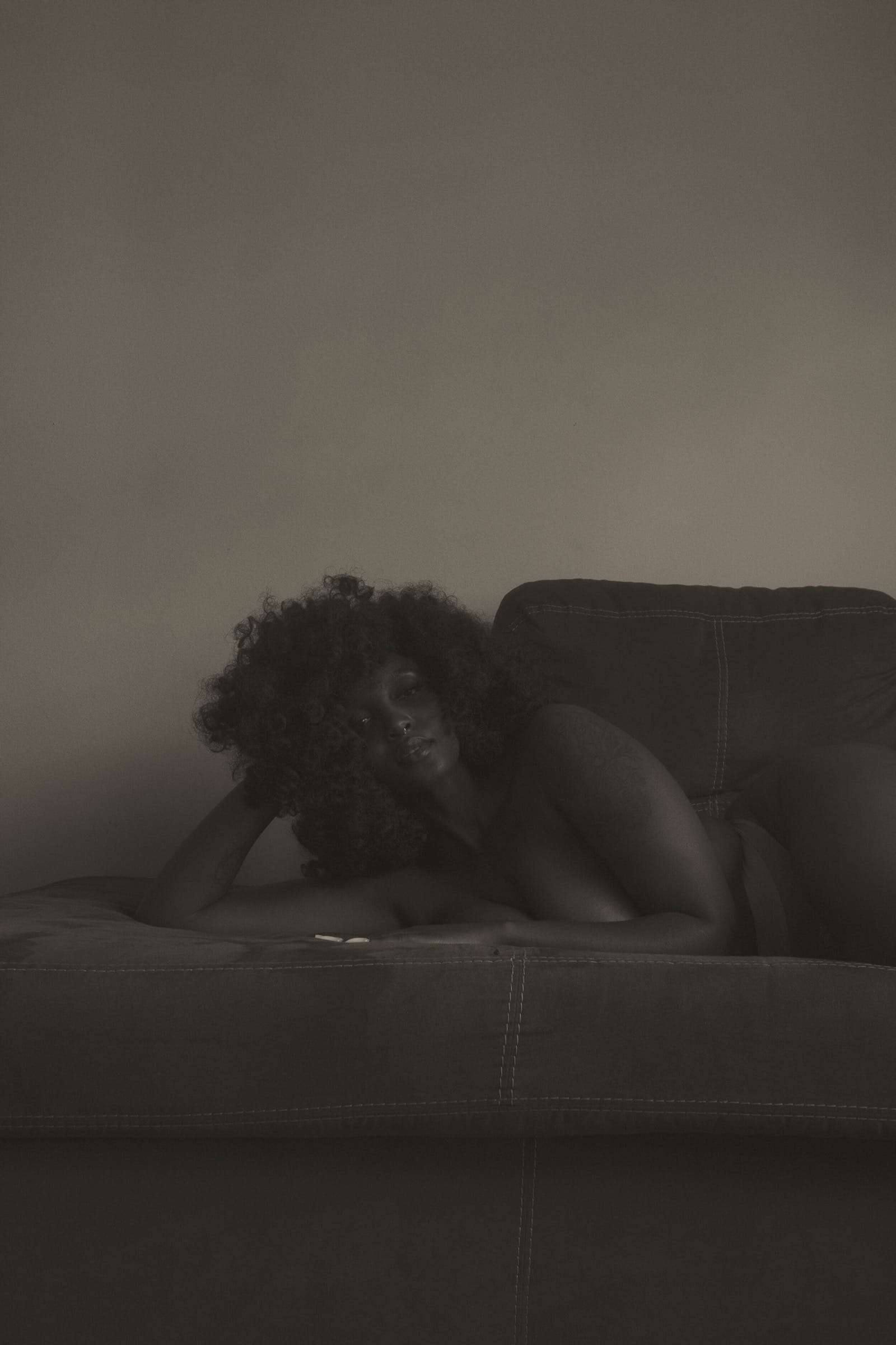 A woman lying on a sofa in a dim room, her head on her arm, from Simi, photographed by Deun Ivory for the body