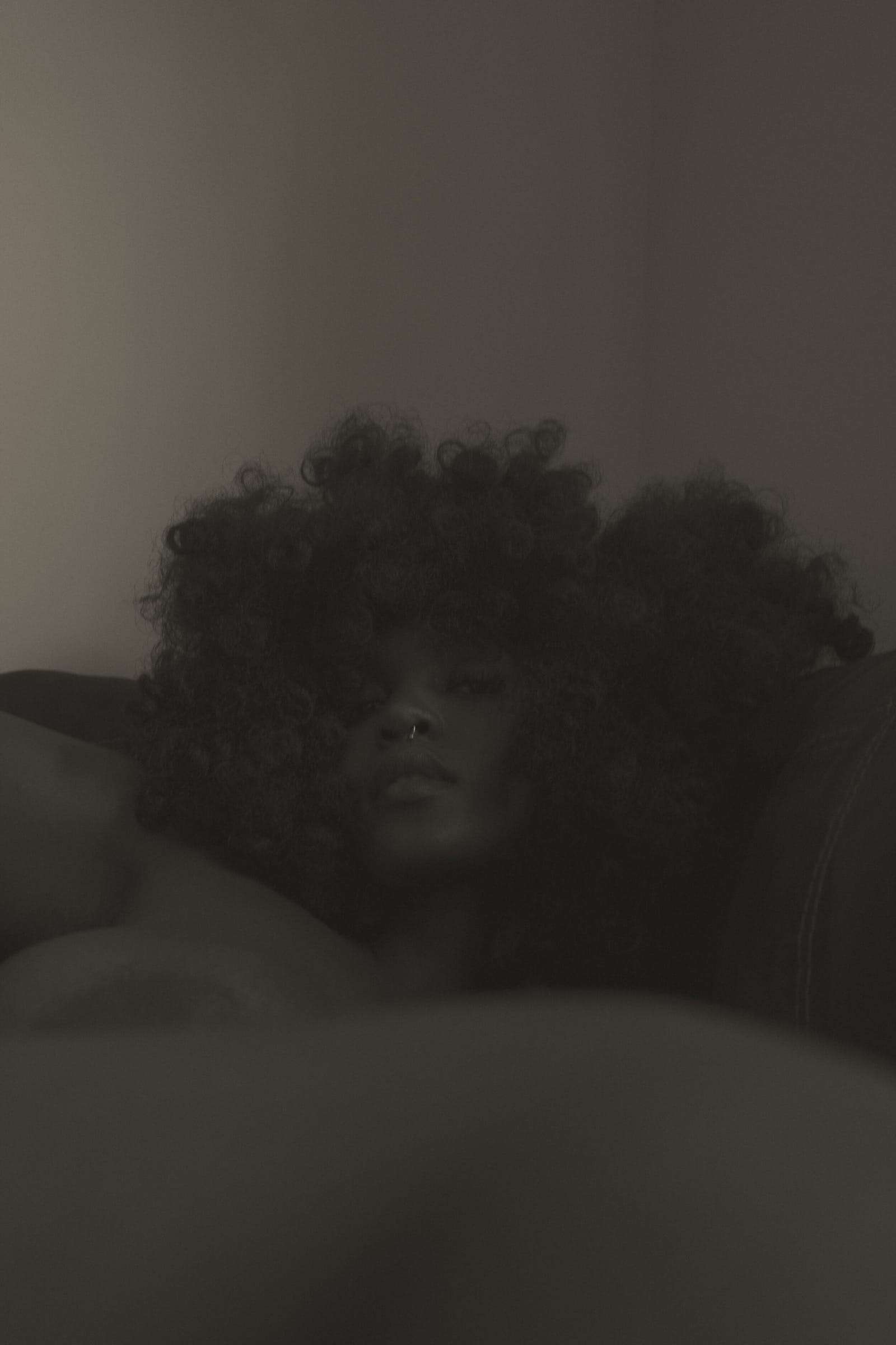 A woman’s face half hidden by her hair, in dim light, from Simi, photographed by Deun Ivory for the body
