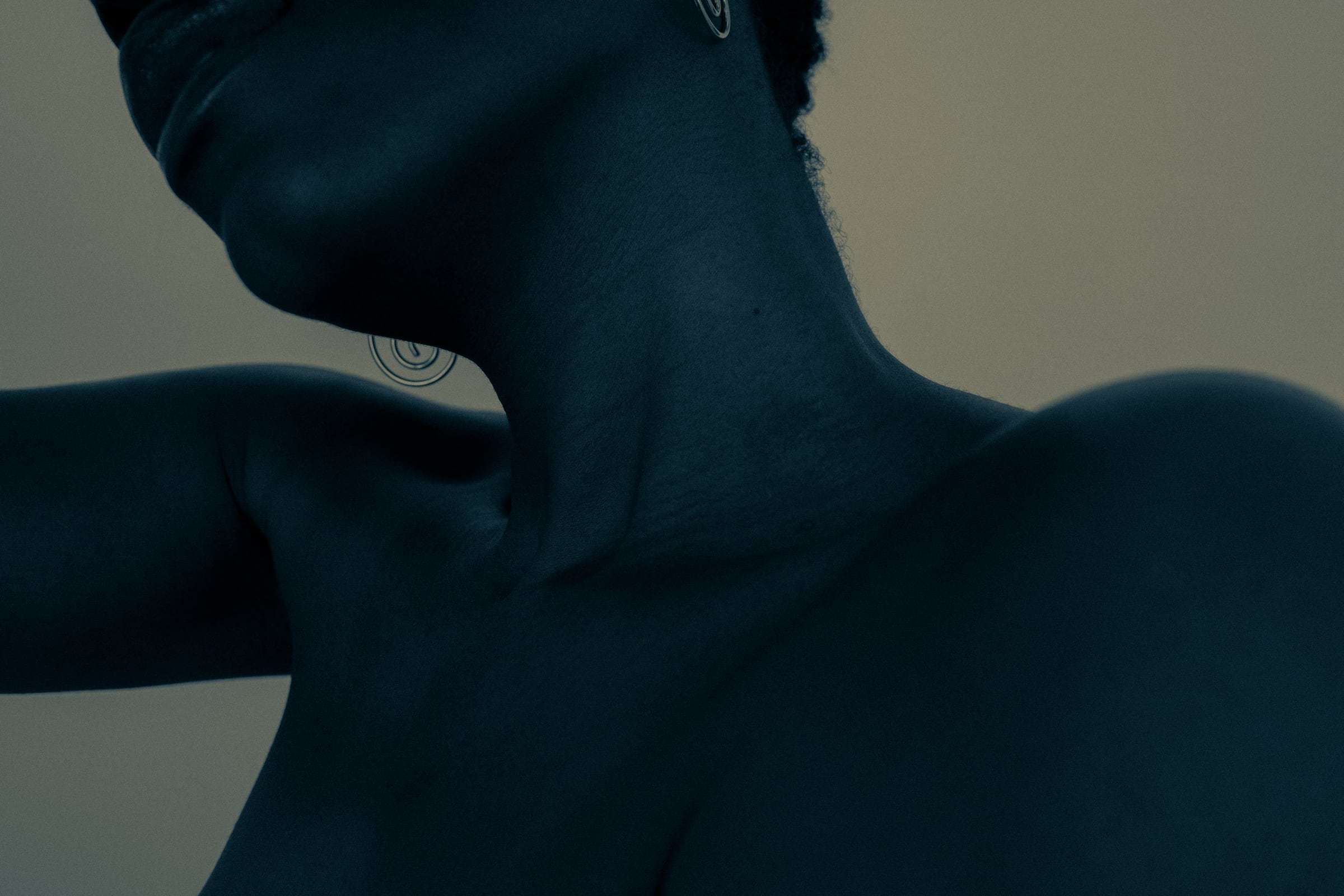 A close crop of a neck and shoulder in blue light, from Deun Ivory’s campaign for Youth To The People