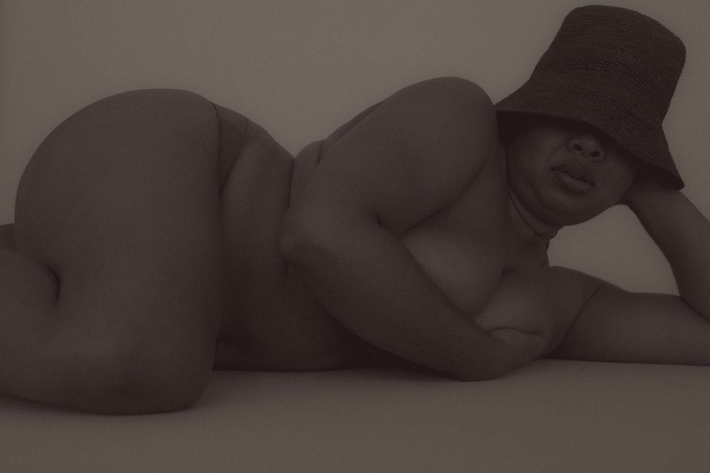 A woman in a bucket hat lying on her side, in soft brown light, from Deun Ivory’s 2024 campaign for Youth To The People