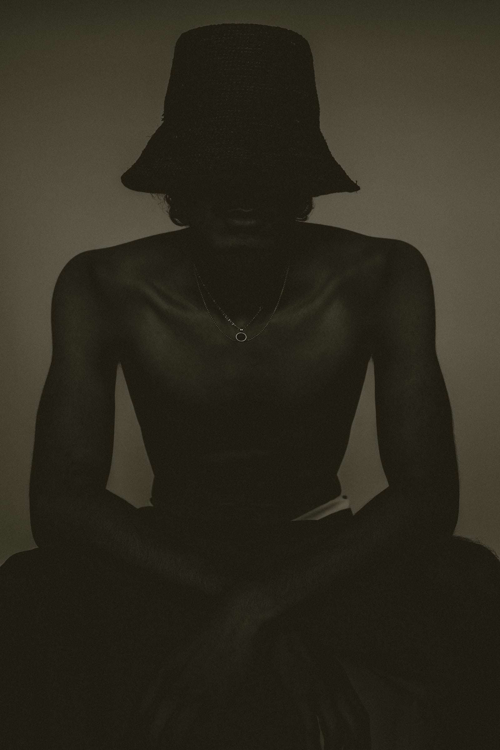 A man in a bucket hat, seated in shadow, from Deun Ivory’s 2024 campaign for Youth To The People